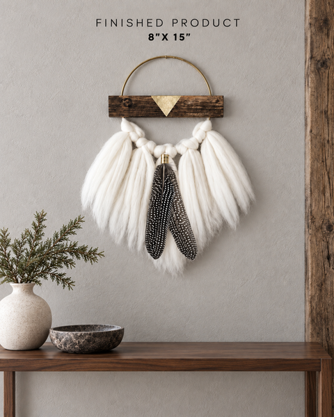 Finished 8” × 15” DIY wall hanging with ivory Merino wool, a brass hoop, wood accents and speckled feathers above a walnut console.