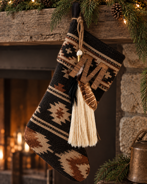 Timber & Torch Boho Tassel with ivory fiber fringe, layered natural feathers and dark wood accents hanging from a black and ivory Southwestern patterned Christmas stocking on a rustic holiday mantel.