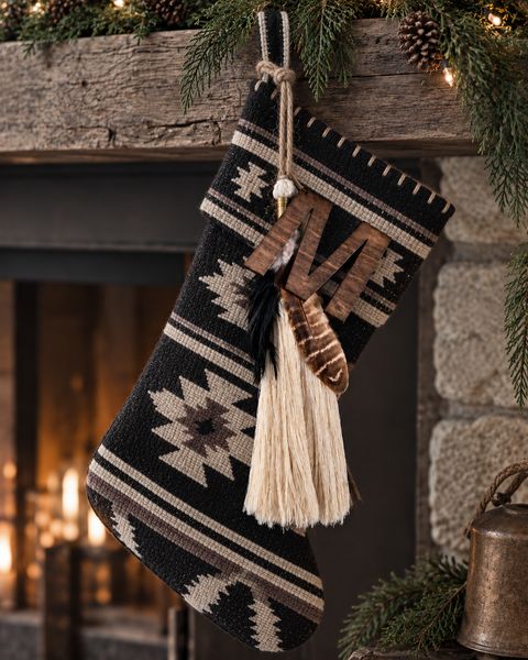 Timber & Torch Boho Tassel with ivory fiber fringe, layered natural feathers and dark wood accents hanging from a black and ivory Southwestern patterned Christmas stocking on a rustic holiday mantel.