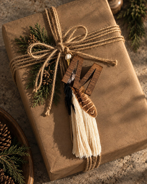 Timber & Torch Boho Tassel featuring ivory fiber fringe, layered natural feathers and dark wood details, styled on a rustic kraft gift box tied with jute and evergreen sprigs.