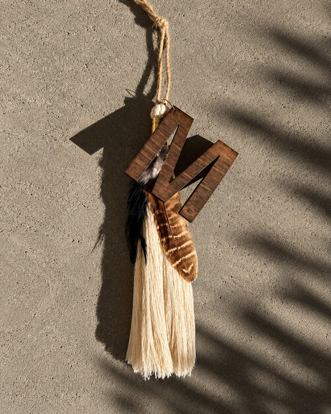 Timber & Torch Boho Tassel with ivory fiber fringe, layered natural feathers and dark wood accents styled as a rustic gift topper on a kraft paper box tied with jute and evergreen sprigs.